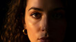 © ANMZAKARIA - Intense close-up portrait of woman with dramatic golden side lighting | High contrast beauty shot focusing on brown eyes and skin texture | Mysterious female model illuminated by warm studio light | A