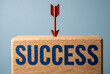 © Ajay - Success target concept with red arrow hitting wooden block typography on blue background for business goal achievement.