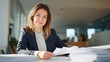 © Elen Nika - Confident young businesswoman smiling while handling paperwork at large white desk in modern corporate office. Successful business leadership, positive professional attitude, female executive portrait