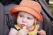 © splitov27 - Little baby in hat sits in a stroller and eats cookies outdoors