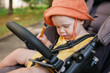 © splitov27 - Little baby in a hat sits in a stroller and looks at a smartphone outdoors
