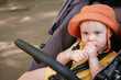 © splitov27 - Little baby in a hat sits in a stroller and eats stick crackers outdoors