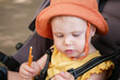© splitov27 - Little baby in a hat sits in a stroller and eats stick crackers outdoors