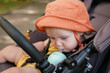 © splitov27 - Little baby in a hat sits in a stroller and drink water from bottle outdoors