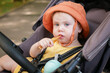 © splitov27 - Little baby in a hat sits in a stroller and eats stick crackers outdoors