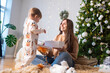 © Ruslan Russland - Happy young woman opening gifts with baby boy in living room near Christmas tree at home.