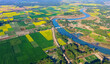 © 光画社 (Kōgasha) - An aerial view shows a river curving through the countryside, bordered by patchwork farmland where mustard crops in full bloom