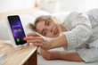 © New Africa - Woman turning off alarm clock on smartphone in bed indoors, selective focus