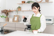 © buritora - Young Asian woman in an apron making coffee in the kitchen