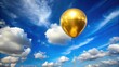 © chokdeelaw - A shiny gold balloon floats in mid-air against a bright blue sky with fluffy white clouds on a sunny day for festive celebrations