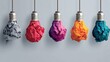 © hen - Five hanging lightbulbs wrapped in colorful crumpled paper nests against a pale blue background, featuring orange,