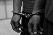© and - Close-up of a prisoner’s hands in modern handcuffs while being escorted to court. Concept of law enforcement, justice system, and criminal trial.