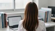© McClerish - Rear view of a young woman working on a laptop at a desk surrounded by books.