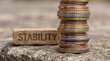 © MYKHAILO KUSHEI - A precarious tower of mixed Euro currency rises beside a small block displaying the word Stability, both resting on a textured stone surface.