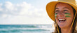 © PhotoGranary - Happy woman with green and gold face paint celebrating Australia Day on the beach. Smiling young female fan in a yellow hat enjoying the national holiday by the ocean with copy space.