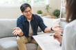 © KMPZZZ - Psychology, depression. smile asian young male, man patient mental sitting on couch, explained symptom with psychologist, psychiatrist while doctor woman taking notes at clinic. Encouraging, therapy.