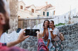 © Novak - Two happy young women posing and having fun while their male friend takes a photo in the old town