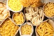 © New Africa - Different types of raw pasta in bags on wooden table, flat lay