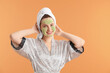 © New Africa - Beautiful woman with cosmetic mask on face and hair wrapped in towel against orange background