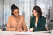 © fizkes - Happy young female Latin business consultant, advisor, agent pointing finger at place for signature for satisfied African client signing contract, agreement, smiling, closing deal, smiling
