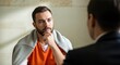 © Mariya Sorvacheva - Male defendant in orange jumpsuit sits thoughtfully with lawyer in suit, discussing legal strategy in a serious atmosphere, conveying the defense process in court