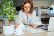 © Soloviova Liudmyla - Beautiful middle-aged woman in glasses thinking about family business budget gazing at monthly bills and documents at home living room office. Small business home finances, money savings concept image