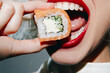 © VICHIZH - Stylish woman enjoying sushi with vibrant red lipstick and a playful expression on her face, highlighting delicious sushi flavors.