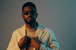 © SHOTPRIME STUDIO - Stylish young African man in sunglasses and a sweater posing confidently against a pastel background, showcasing modern fashion and self expression
