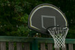 © Viktar - Neighborhood basketball hoop under soft dusk with rusty rim and swaying net, chainlink fence backdrop and dark trees, gritty asphalt court evoking urban pickup energy, late evening training vibe