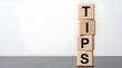 © alvi - Stacked wooden blocks spelling 'TIPS' on a gray surface against a white background with a shallow depth of field.
