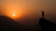 © dmmarychev - Silhouette of a man with raised arm standing on a mountain peak at sunset