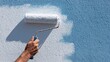 © dmmarychev - Close-up of a hand using a paint roller to cover a blue wall with white paint
