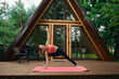 © boomeart - Woman practicing yoga on a pink mat outside a wooden cabin in the woods during daytime