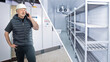 © Grispb - Industrial refrigeration, cold storage facility. Engineer in a hard hat inspects cooling equipment and empty refrigerated shelves, coordinating installation, maintenance, and temperature control.