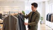 © Vasiliy - A young Asian man shopping for a suit in a modern clothing store. Happy male customer choosing a new jacket in a menswear boutique.