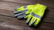 © Anastasiya Marchenko - Pair of high-visibility yellow and gray work gloves with reflective strip lying on rustic wooden surface