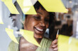 © Xavier Lorenzo - Young African American businesswoman evaluating her creative strategies and new ideas, writing on yellow sticky notes attached to a clear glass wall in a modern office setup. Business concept