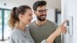© Formoney - A couple stands close together in their house. They smile while one partner points at the thermostat control. Sunlight fills the room.