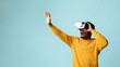 © Prostock-studio - Young african american guy in casual using VR glasses, touching something invisible at copy space, millennial black man experiencing virtual reality adventure on blue studio background, panorama
