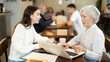 © JackF - Elderly woman typing on a laptop and carefully communicating with a young woman in a cafe. Business meeting of two women of different ages in a coffee shop