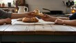 © Zuhri - Two people sharing a piece of freshly baked bread at a rustic wooden table.