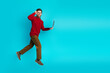 © deagreez - Young man in red sweater leaps with a laptop against a blue background for dynamic lifestyle and modern business promotion in fashion advertising