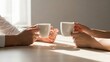 © Image - Two people clinking white coffee mugs in a warm, sunlit setting, enjoying a beverage together.