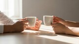 Two people clinking white coffee mugs in a warm, sunlit setting, enjoying a beverage together.