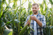 © Serhii - Farmer examining corn cob in cultivated field at sunset