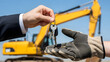 © Felipe - Mano entregando llaves con maquinaria de construcción al fondo, concepto de alquiler, entrega, compra y gestión de activos industriales