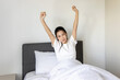 © Stella - Beautiful sleepy Asian woman waking up in bed, stretching her arms in the morning. Young pretty female sleeping on comfortable bed and trying to wake up. A woman stretching lazily after waking up.