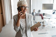 © Jelena - Senior Woman in Office On Phone With Notebook, Smiling, In Professional Attire