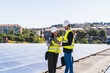 © Koldo_Studio - Two engineers with hard hats and safety vests inspecting a large solar panel installation on a rooftop, focusing on renewable energy