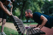 © qunica.com - Outdoor fitness scene with adults pushing a bench in a park. A group exercises together, using a bench for strength training.